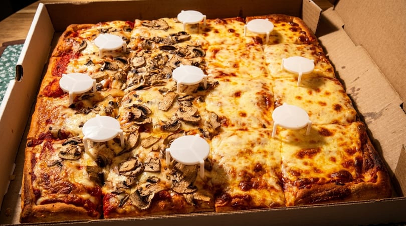 A rectangular pizza in a box, half cheese and half mushroom, with pizza savers.