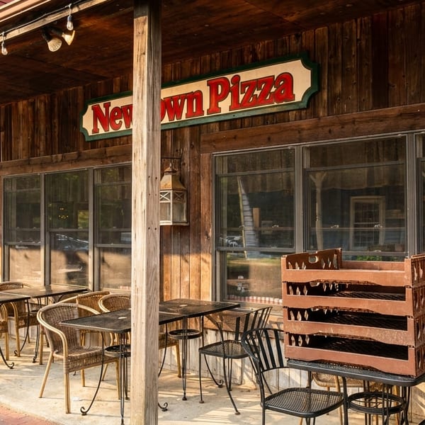 Newtown Pizza restaurant exterior with a wooden facade, outdoor seating, and a red and white sign.